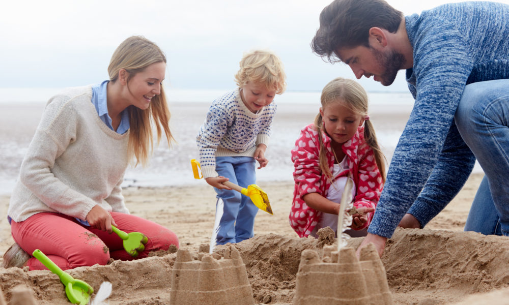 A family on the beach building sandcastles with their children.